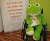 Rollup mit Kuscheltier-Frosch als Maskottchen für den Verein INDD sitzend im Rollstuhl und den Karten für die Karrierestart 2018