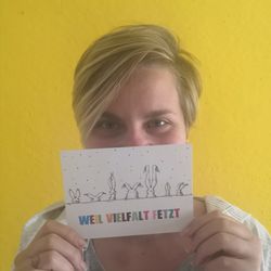 Frau mit kurzen Haaren hält Hasen-Postkarte vom INklusionsnetzwerk vor die Nase mit der Aufschrift Weil Vielfalt fetzt