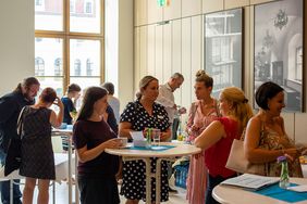 Frauen und Männer stehen um Stehtische und reden