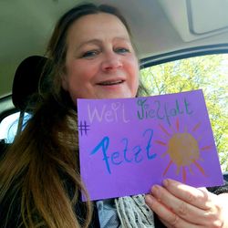 Frau im mittleren Alter mit braunen langen Haaren zeigt lila Papierschild: Weil Vielfalt fetzt