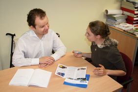 LSKS_Beratung Beratungsszene - Mann und Frau im Gespräch, davon einer mit Gehhilfe sitzend am Tisch