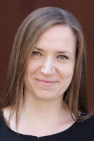Profilbild von Kerstin Helm - sie hat lange dunkelblonde Haare, steht vor einem roten Hintergrund und lächelt in die Kamera